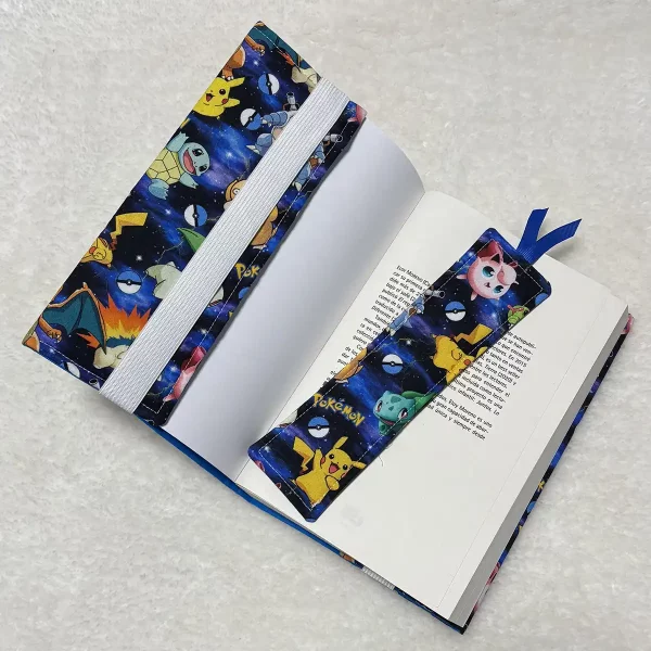 Funda de tela artesanal abierta sobre libro, mostrando el elástico de sujeción y un marcapáginas a juego con cinta decorativa.
