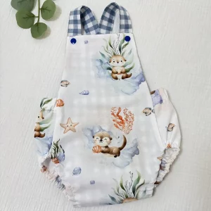 Ranita de bebé artesanal con tirantes de cuadros azules y fondo blanco, confeccionada en algodón con diseño marino y botones a presión azules.