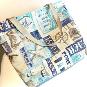 Bolsa de playa grande con estampado marino en tonos azules y beige, con asas de algodón resistentes, ideal para llevar todo lo necesario en días de verano.