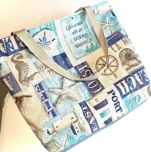 Bolsa de playa grande con estampado marino en tonos azules y beige, con asas de algodón resistentes, ideal para llevar todo lo necesario en días de verano.