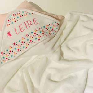 Capa de baño para bebé en color blanco con borde estampado de estrellas y nombre ‘Leire’ bordado a mano en hilo rosa