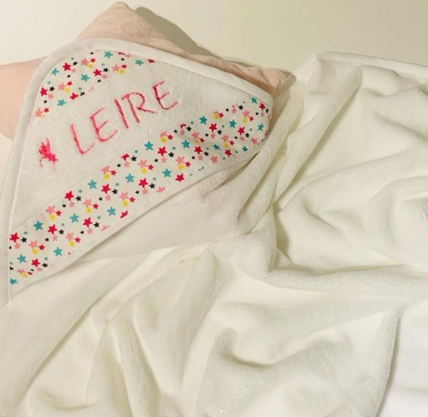 Capa de baño para bebé en color blanco con borde estampado de estrellas y nombre ‘Leire’ bordado a mano en hilo rosa