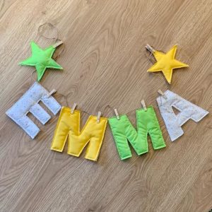 Guirnalda de tela personalizada con el nombre 'Emma', en tonos amarillo, verde y blanco con detalles de estrellas, hecha a mano con materiales suaves y ecológicos.