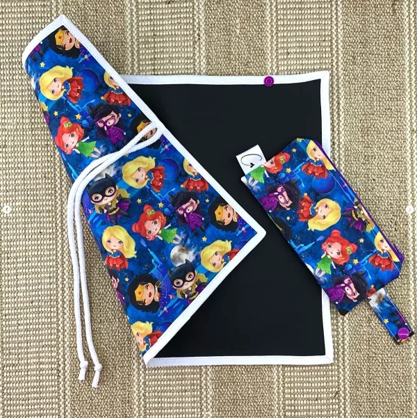 Pizarra infantil con diseño de superheroínas en tonos vibrantes. Superficie reutilizable y cierre con cuerda.